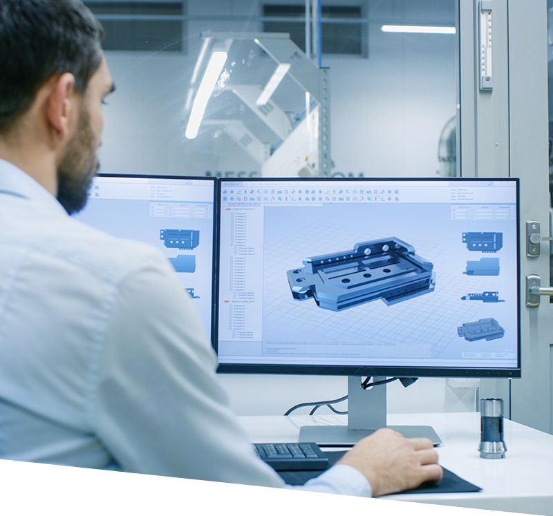 Engineer/ Technician Working on a Personal Computer with Two Displays, He's Designing New Component in CAD Program. Out of the Office Window Components Manufacturing Factory is Seen.